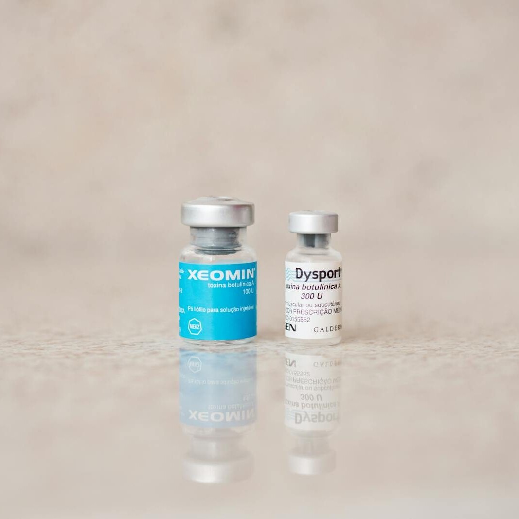 Close-up of Xeomin and Dysport bottles reflecting on a surface, shot indoors.